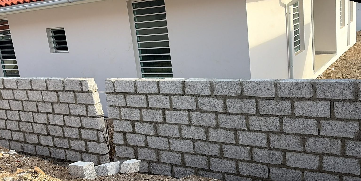 Concrete block garden wall beside a white house with red roof tiles